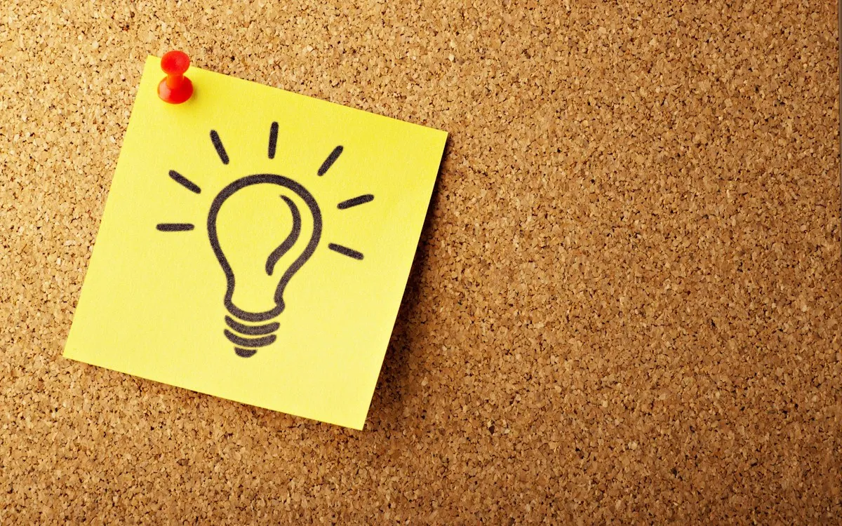 Yellow sticky note with a hand-drawn light bulb pinned to a cork board