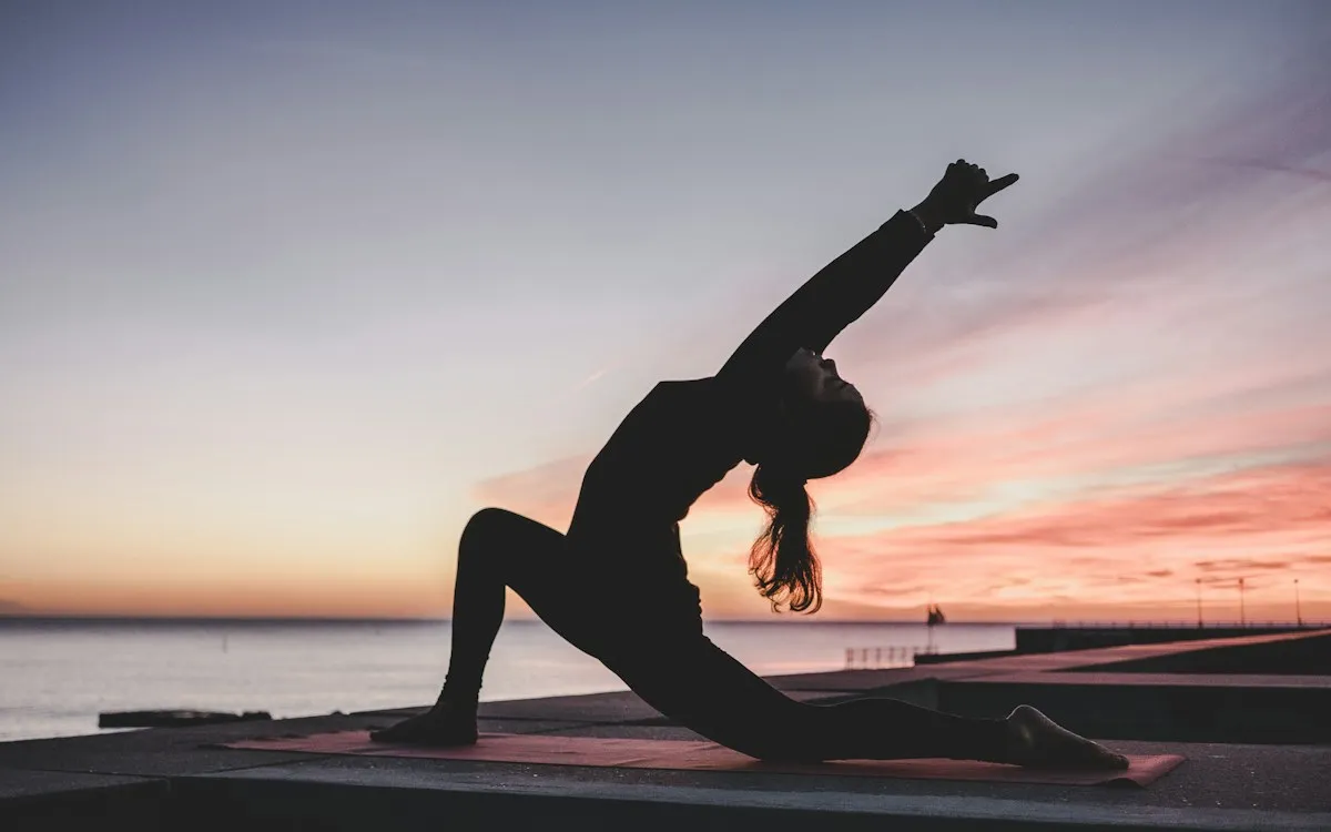 Silhouette of a woman in a yoga pose against a pink sunset sky