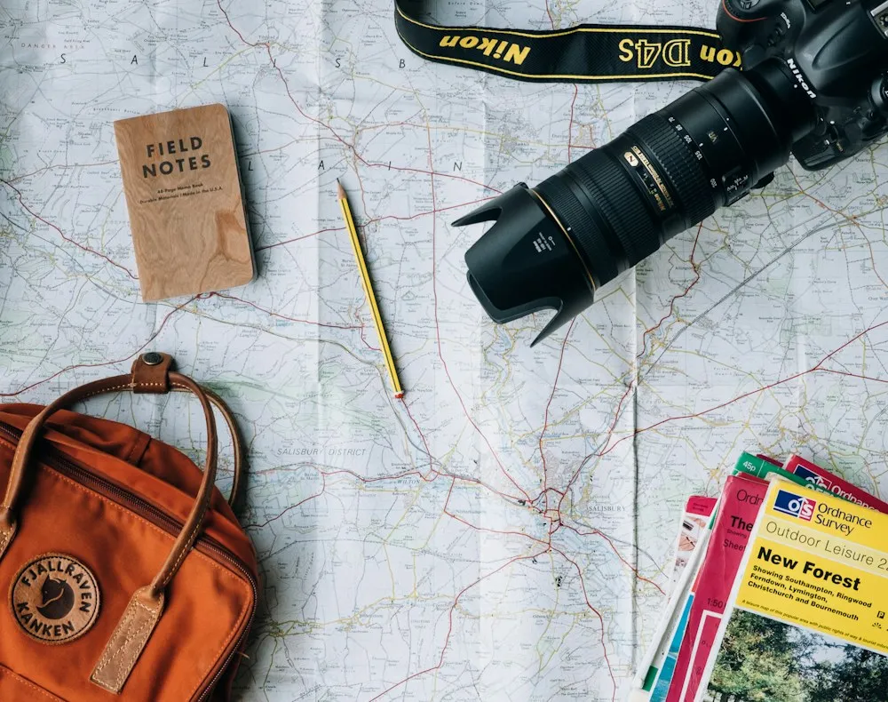 Map, camera, notebook and backpack laid out on a table for trip planning