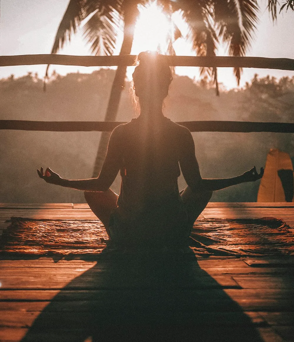 Person meditating at sunrise on a wooden deck